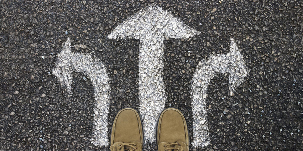 A person standing before a road sign with three arrows pointing in different directions.