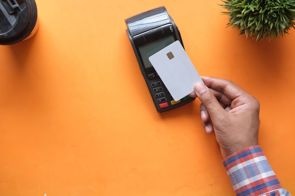 A hand holding a card over a POS in an orange background.