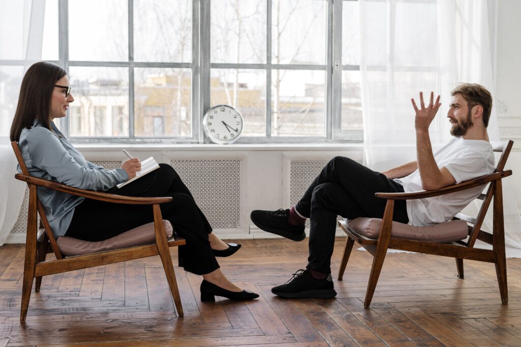 A therapist and a patient engaged in conversation while seated on chairs.