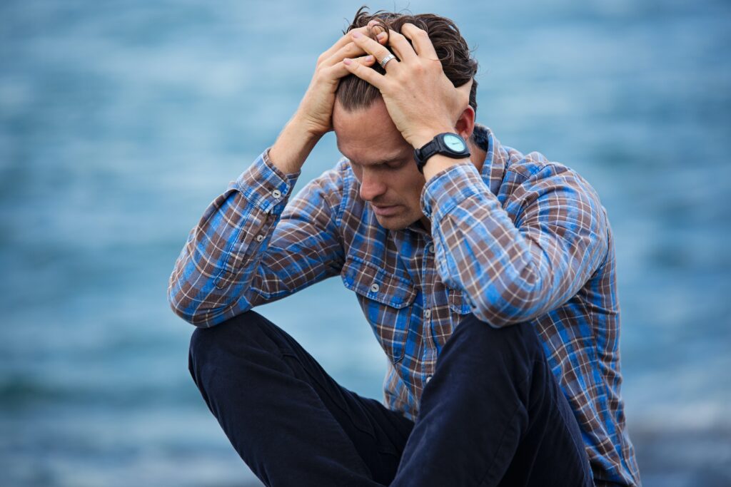A man sitting on the ground with his head in his hands, looking distressed.