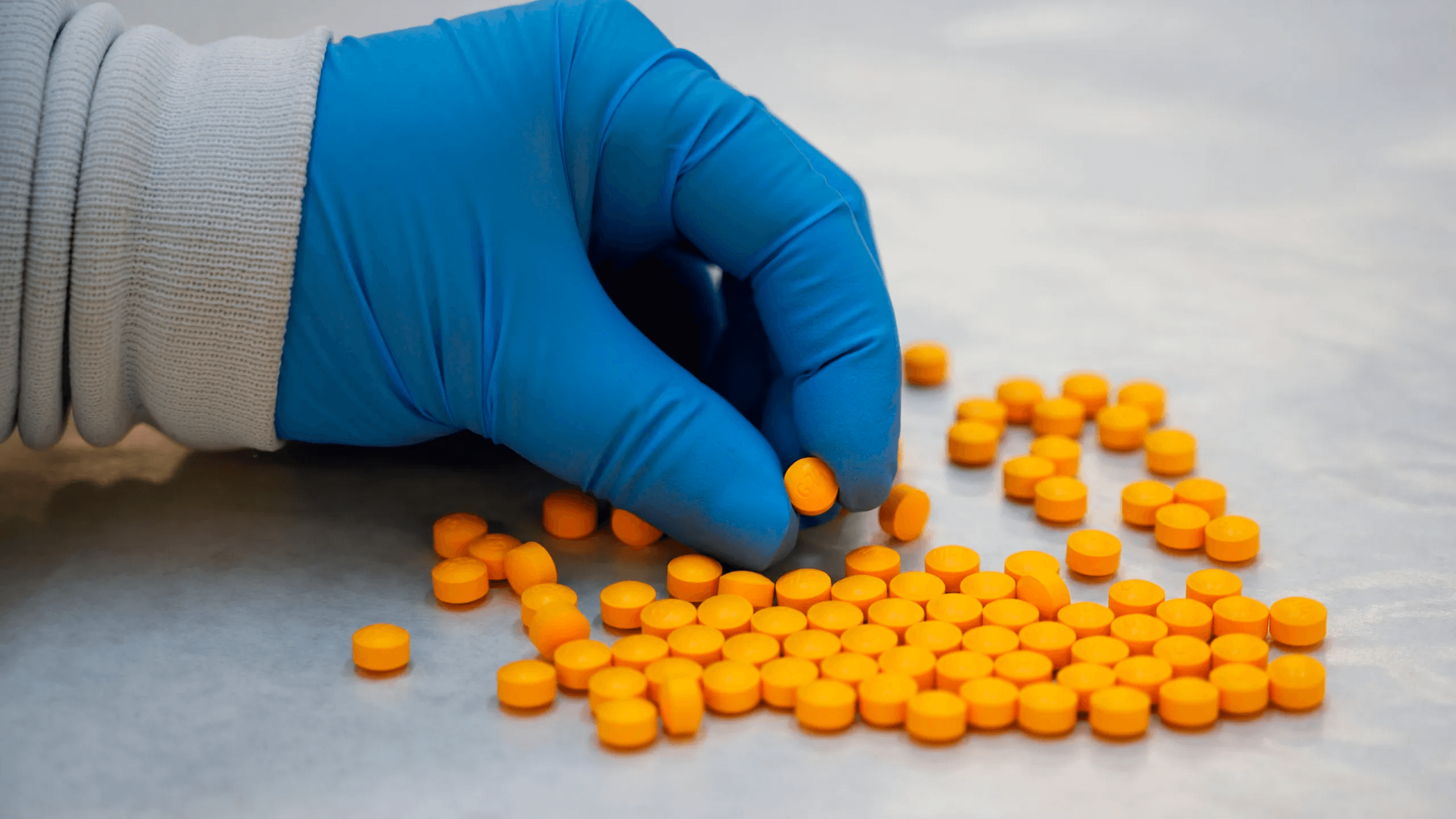 A hand in blue glove holding a pile of orange pills.