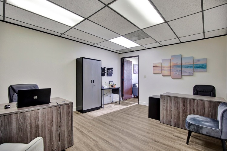 Zoe Behavioral Health's tidy office space has a desk, two chairs, and wall paintings, and it is ready for work or meetings.