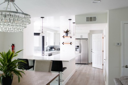 A modern kitchen viewed from a dining area featuring white cabinets, stainless steel appliances, and pendant lighting.
