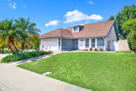 A house surrounded by lush green grass and tall palm trees.