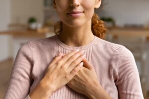 Woman in a pink shirt hold her hands close to her heart while repeating affirmations