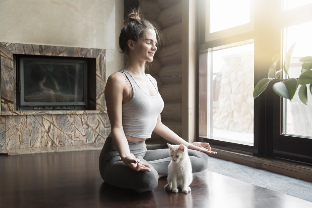 Woman meditating cross-legged with her pet cat beside her