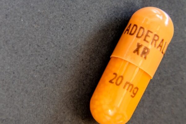 Single orange and white Adderall capsule on a table