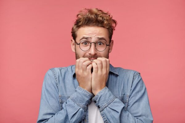 Man biting his fingers in anxiety with pink background