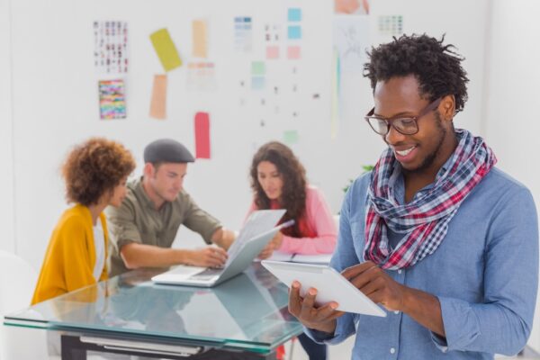 Young man in the office looking at a smart tablet with colleagues behind him