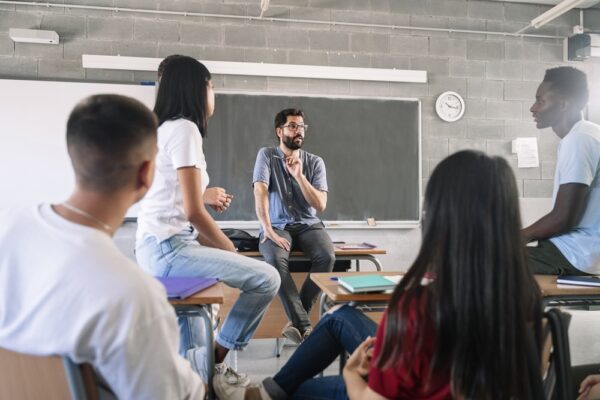 Teens listening to a teacher inside a classroom during an informal discussion about drug prevention