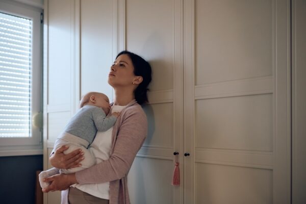 Mother holding her newborn baby  looking upset leaning on a cabinet