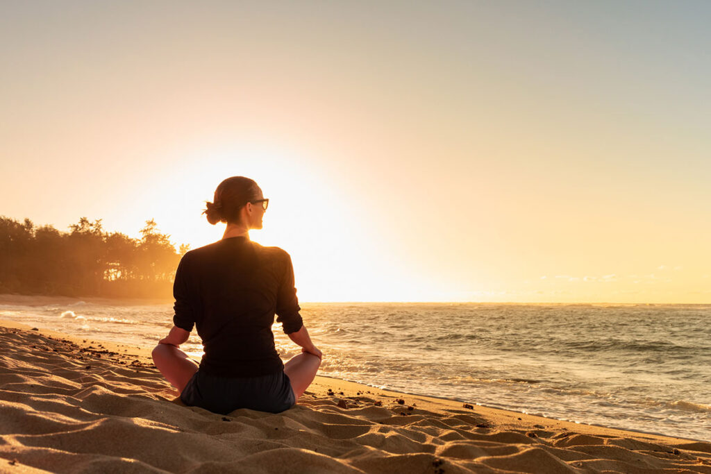 Young woman looking out to the ocean sunrise finding peace happiness in nature.