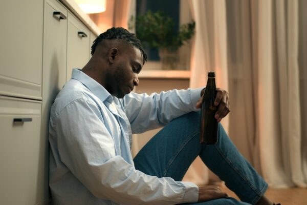 Adult male sitting on the floor holding a beer bottle who relapsed due to a romantic relationship