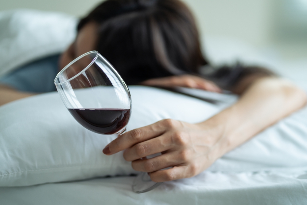 Drunk woman in bed holding a wine glass