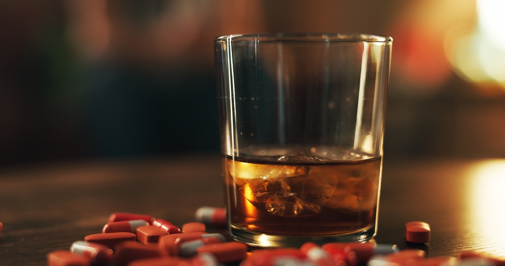 Scattered Adderall pills on the table with a glass of alcohol in the middle