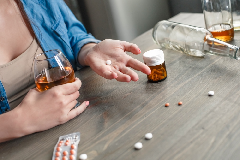 Woman holding a white pill on her hand with a glass of alcohol on her other hand