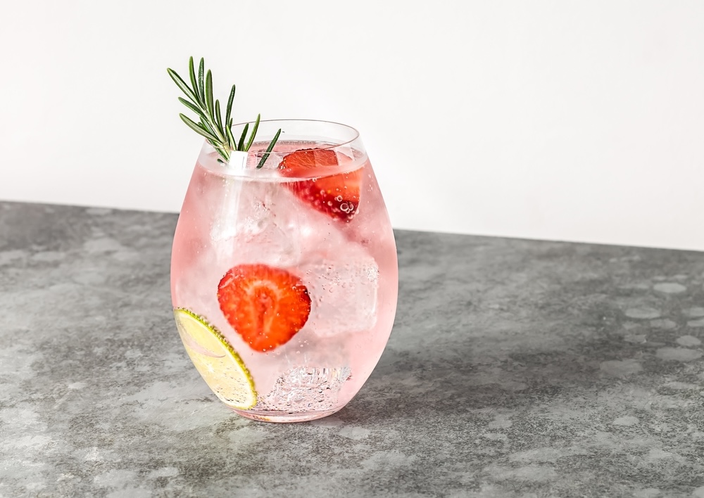 Pink Whitney on a clear glass with strawberry slice and rosemary twig