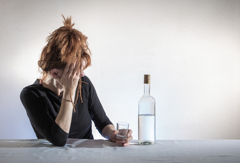 Woman feeling tipsy after drinking vodka from a bottle