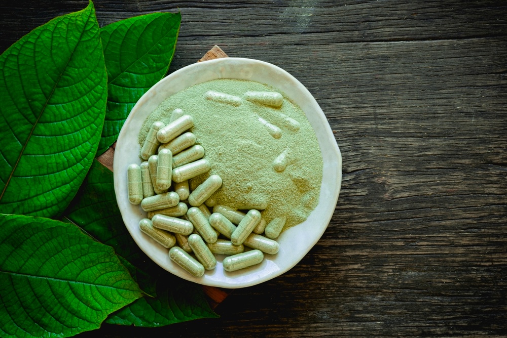 White bowl with Kratom capsule and powder surrounded by Kratom leaves