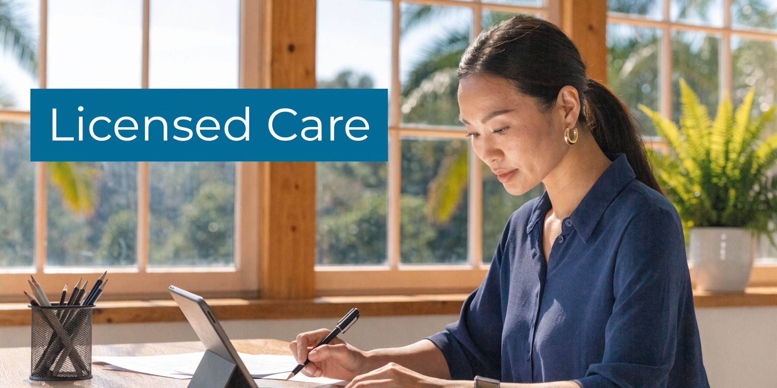 A professional woman in a bright office focusing on paperwork while working on her digital tablet device.