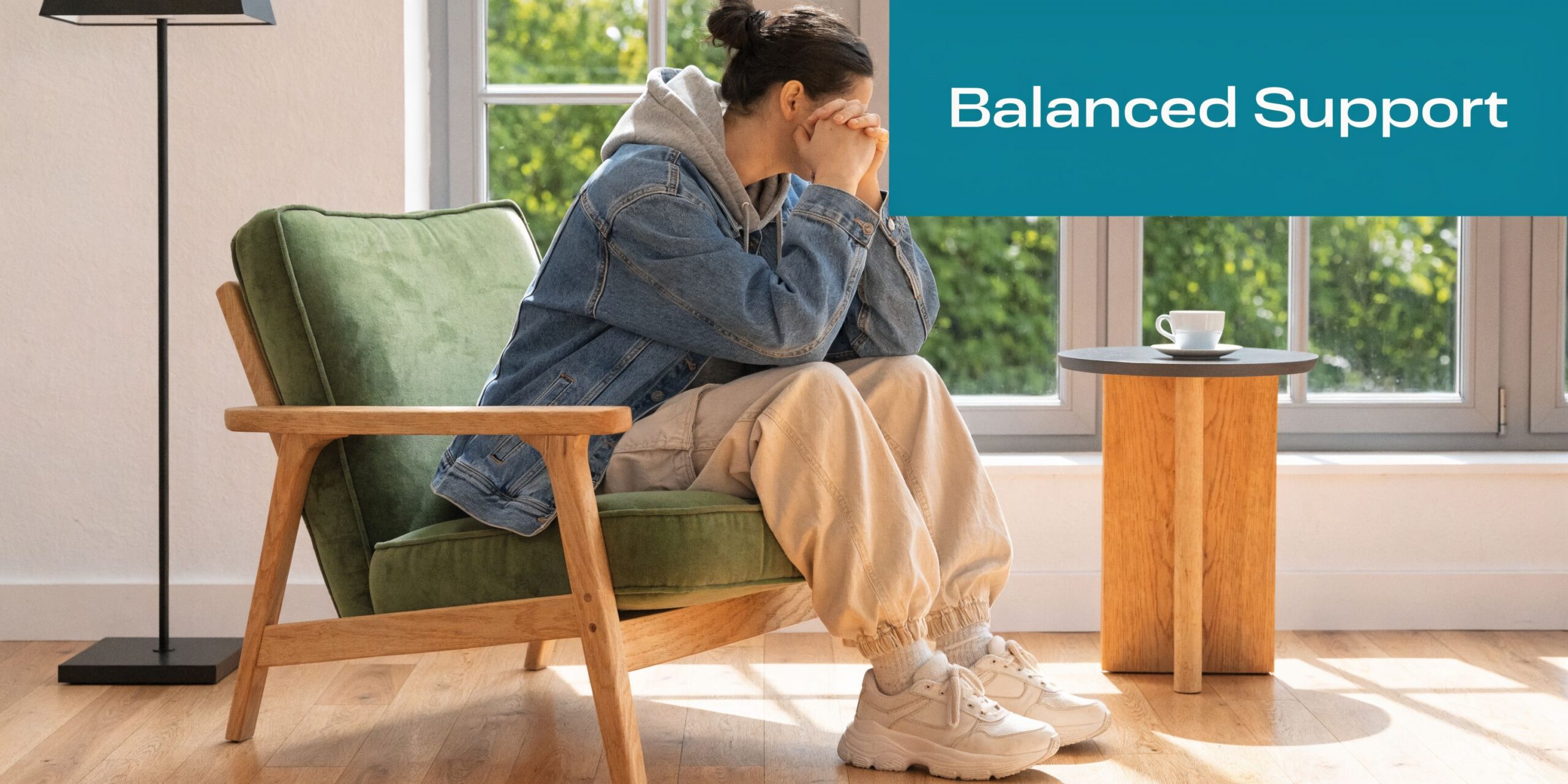 A person sitting in a green chair with their head in their hands, representing mental health support.