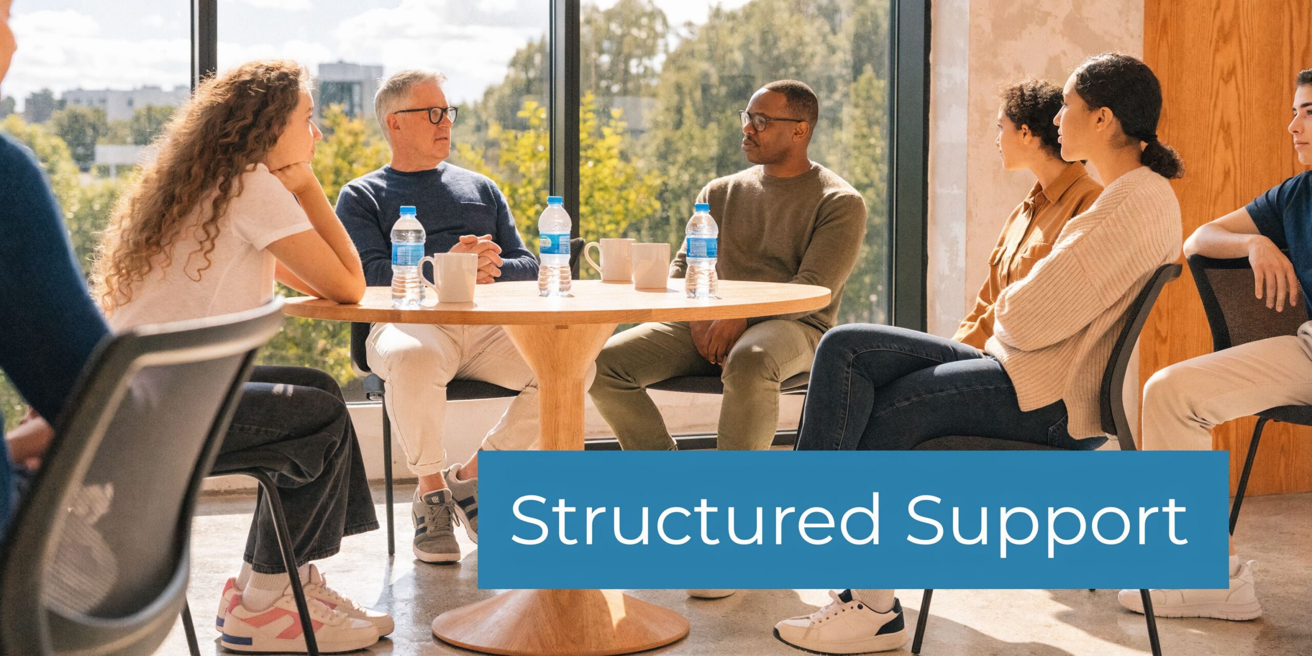 A diverse group of people sitting around a table having a discussion in a support group setting.