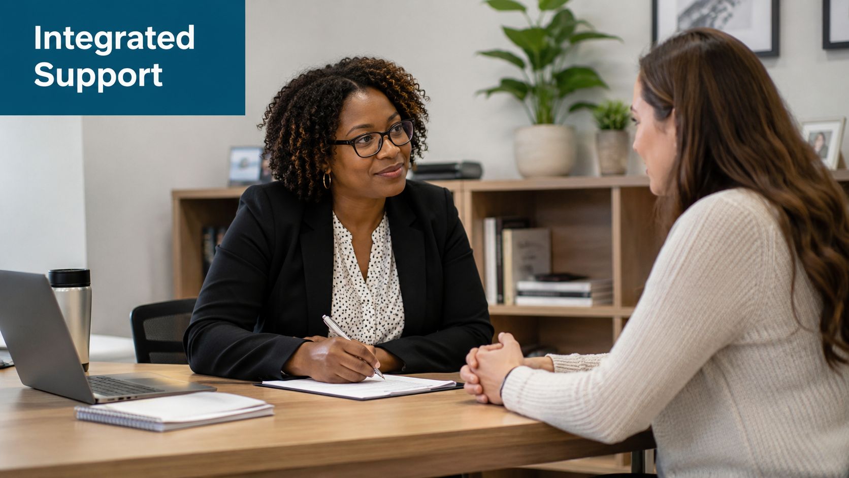 A professional woman in a business suit writing on a document while consulting with another woman.